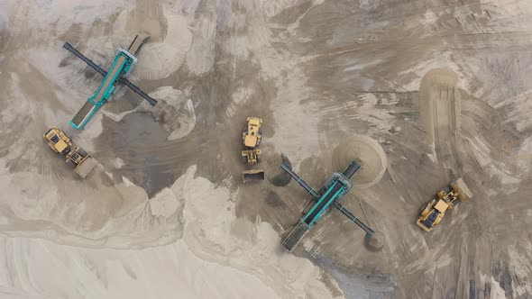 Top aerial view of bulldozer loading sand into empty dump truck in open air quarry. alt
