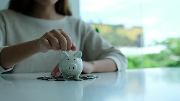 a woman putting coin into piggy bank with pile of coins on the table for saving money