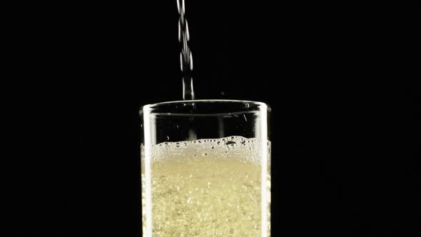 Sparkling Yellow Water is Pouring Into Wineglass Standing on Black Background alt