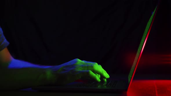 Closeup Man Sitting Table Notebook. Hands Keyboarding Laptop Green Screen. Neon Glow of Blue, Red. alt