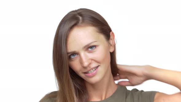 Portrait of Caucasian Female Wearing Braces Touching Long Brown Hair Looking at Camera and Smiling alt