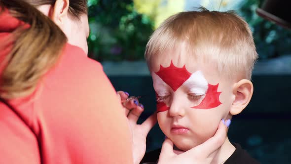 A little boy is put face painting on his face, his face is painted with paint