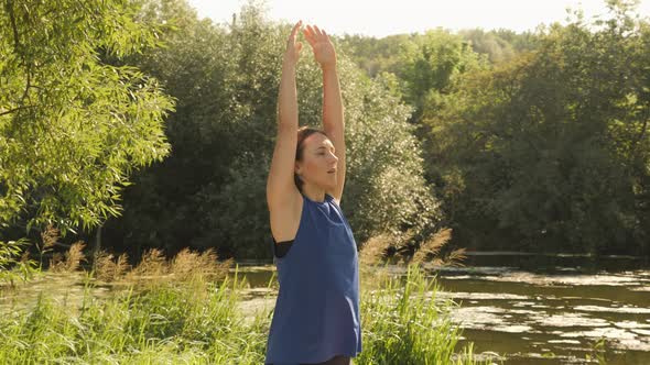 Portrait of woman meditating in park at sunrise. Young serene female practicing yoga and stretching alt
