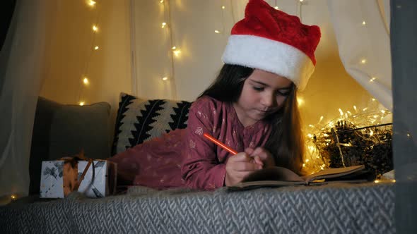Little Girl Writes a Letter to Santa Claus with Wishes Lying on the Windowsill Decorated with a alt