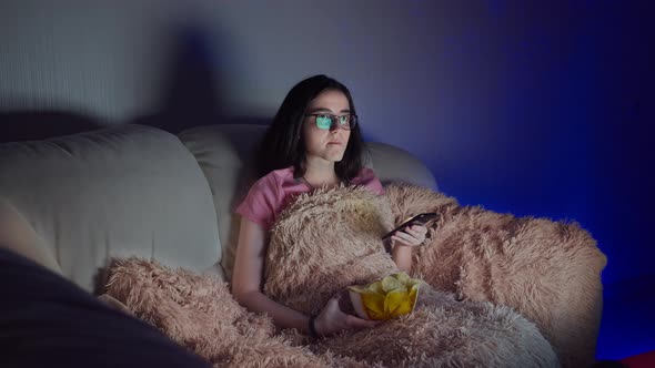 Girl Sitting on the Couch Watching Tv Uses Phone and Eating Chips in the Evening
