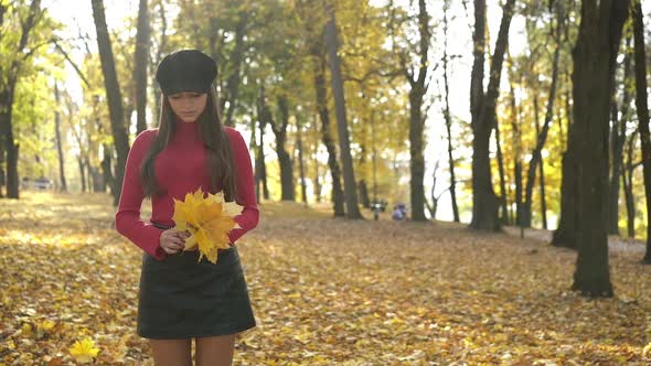 Lady Stands with Maple Leaves and Looks at the Sky in Sunny Autumn Park alt