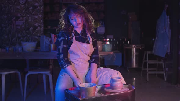 Pottery Crafting Woman with Curly Hair Working with a Fresh New Pot on the Potter's Wheel Looking in alt