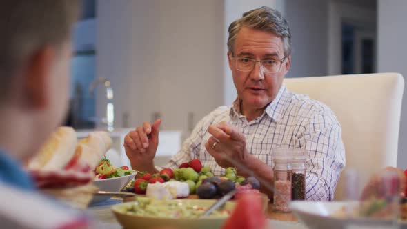 Smiling caucasian grandfather talking to grandson at table during family meal alt