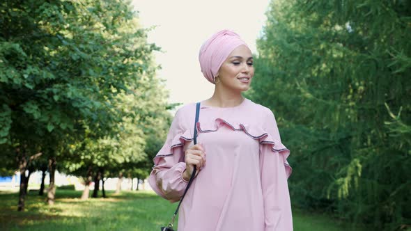 Girl in Long Purple Dress and Hijab Wanders Along Park alt