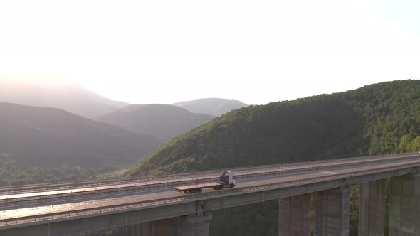Aerial View of Truck with Flatbed Trailer Driving on Highway Viaduct in the Mountains alt