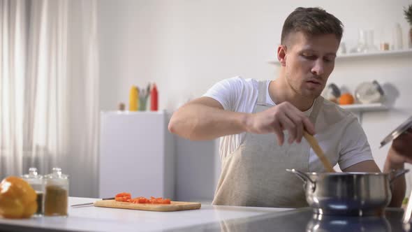 Handsome Young Man Tasting Vegetable Soup, Cooking Healthy Vegetarian Food alt