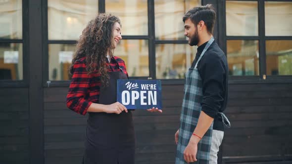 Slow Motion Portrait of Two Happy Entrepreneurs Cafe Owners Posing with Open Sign in Front of New alt
