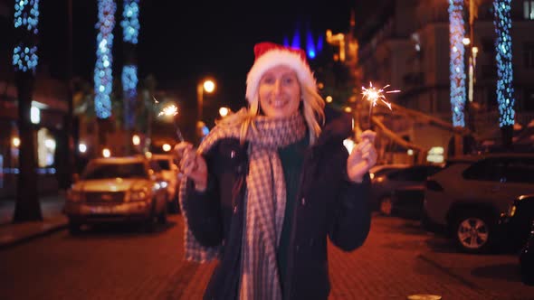 A beautiful woman in a Santa Claus hat walks at night on Christmas alt