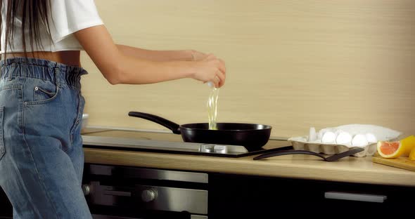 Young Brunette Standing in the Kitchen Breaking Eggs Into a Frying Pan