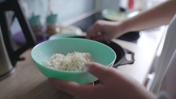 Woman Puts Fresh Steamed White Rice Into Deep Blue Plate with Spoon alt