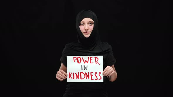 Portrait of Smiling Muslim Woman in Hijab Holding Power in Kindness Sign Looking at Camera alt