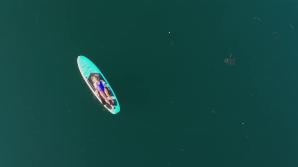 Young Blonde Woman Lying on Surfing Board Female Swimmer Wearing Swimming Suit Relaxing on Blue alt