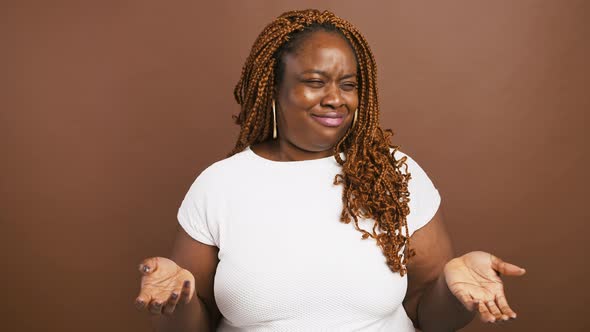 Emotional Incomprehensible Black Woman Shrugging Shoulders and Raising Hands Brown Background alt