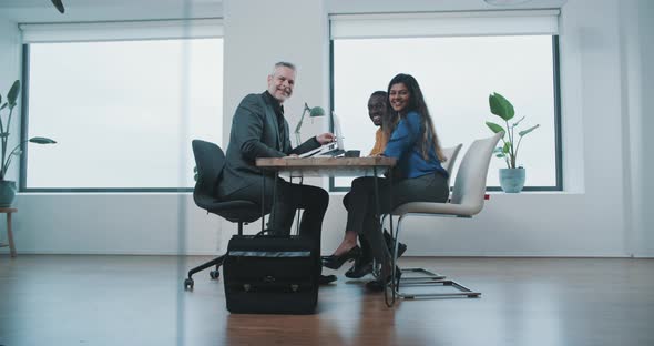 Couple smiling into camera while sitting at a table with realtor to sign contract alt