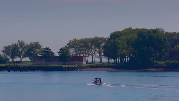 Wide shot of Hart Island on a sunny day. Across the water with a blue sky. The shot follows a speed alt