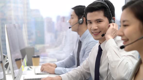Young Asian male telemarketing operator smiling to the camara while working at call center