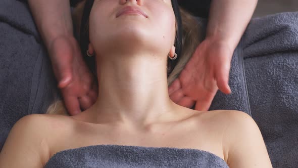 An Attractive Woman Lies on a Bed in a Beauty Salon and Gets a Massage on the Decollete and Neck alt
