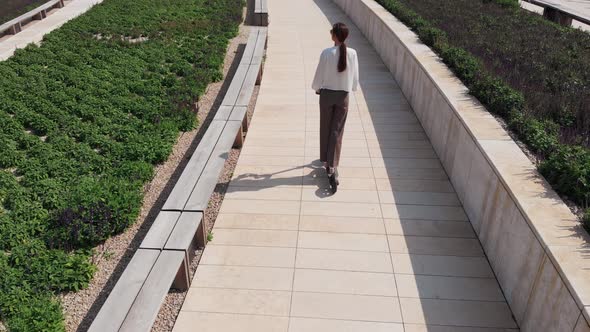 Adult Businesswoman Goes To Work on an Electric Kick Scooter. Drone Tracking Aerial View, Long Shot alt