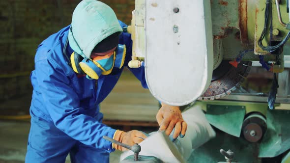 At the factory, a male worker in a protective mask and gloves processes a decorative stone on a mach alt