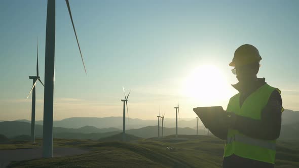 Technician Engineer in Wind Turbine Power Generator Station Standing with a Tablet in His Hands