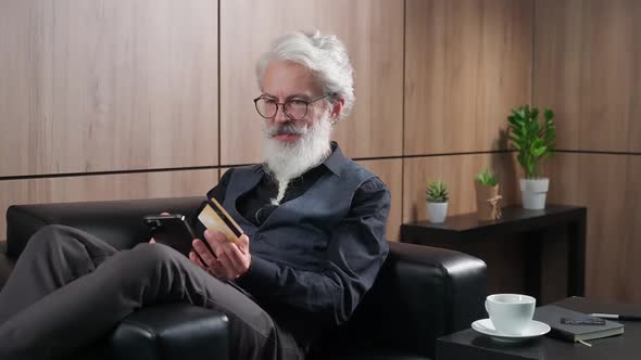 Elegant Grayhaired Man Makes Successful Purchases Online Using a Smartphone and a Credit Card Adult alt