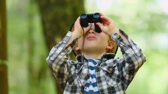 Little blond boy exploring in woods with binoculars