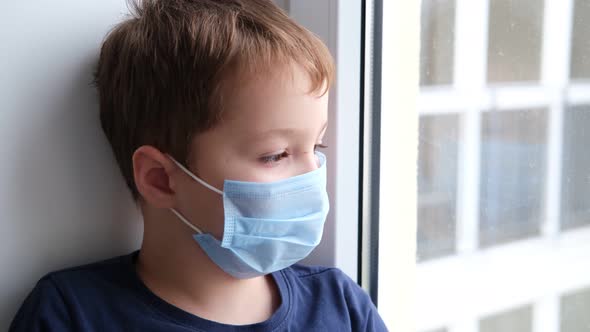 Little Boy in a Medical Protective Mask Sits on the Windowsill