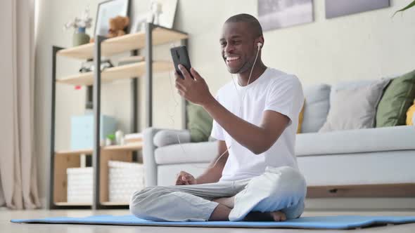 African Man Talking on Video Call While Sitting on Yoga Mat alt