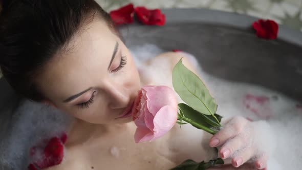 Sexy Girl Lies in a Big Stone Bath with a Rose Flower in Her Hands alt