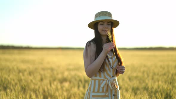 Beautiful Young Woman with a Hat Holds an Ear of Wheat in Her Hands alt