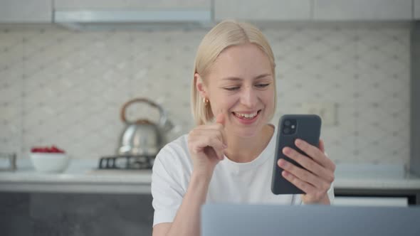 Joyful Blonde Woman Waves Bye in Video Call When Sitting at Laptop in Kitchen