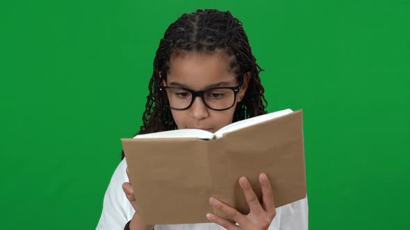 Charming African American Teen Girl in Eyeglasses Reading Book on Green Screen Looking at Camera alt