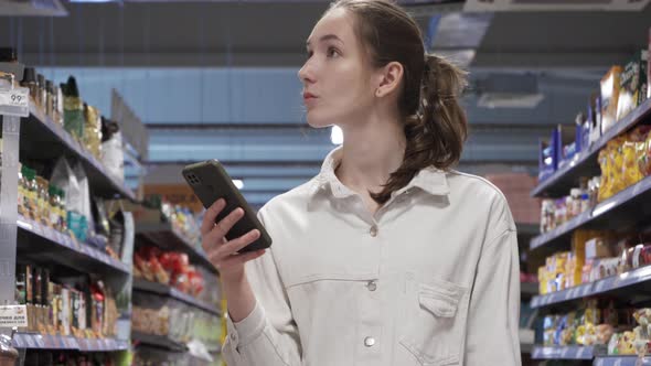 Young Woman Looking at a Smartphone Screen in a Supermarket alt