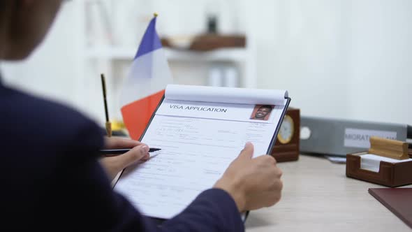 Embassy Employee Approving Visa Application, French Flag on Table, Migration Law alt