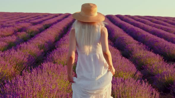 Young Woman in White Dress Walking Through a Lavender Field on Sunset