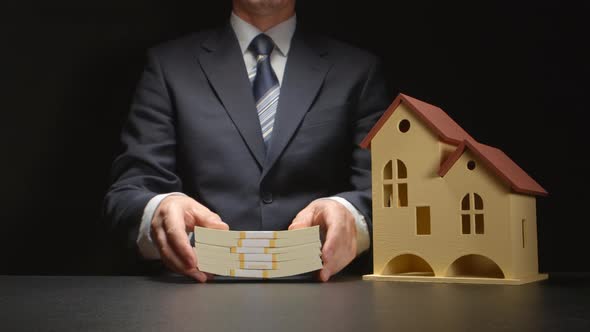 Businessman counts and gives a money and near a house model on a table