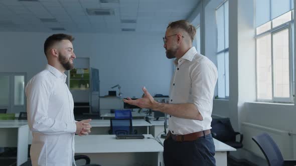 Two Bearded Men in White Shirts Talk in an Office alt
