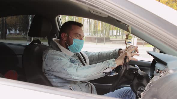 A Modern Young Man in a Mask is Worried Nervous Sitting Behind the Wheel alt