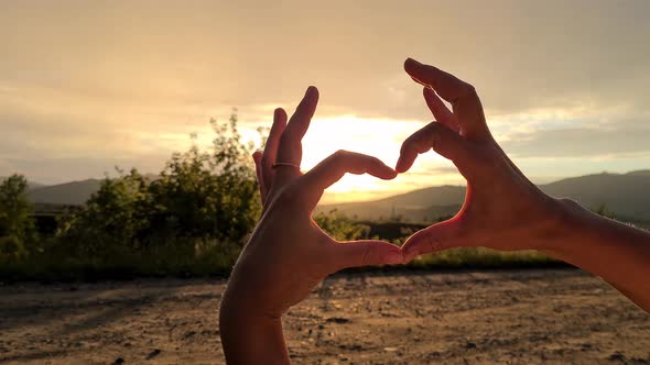 women's hands make a heart at sunset