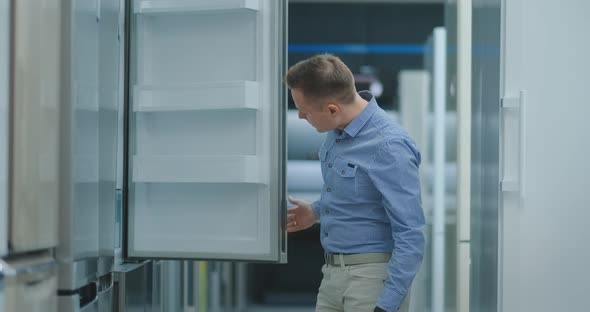 Handsome Man in Blue Shirt Open the Refrigerator Door in Appliances Store and Compare with Other