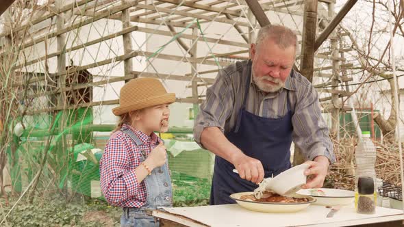 Grandfather and Granddaughter Taste Grilled Meat Kebab From the Grill Grate alt