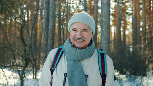 Slow Motion Portrait of Senior Man Smiling Looking at Camera in Winter Forest alt