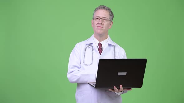 Portrait of Mature Man Doctor Thinking While Using Laptop