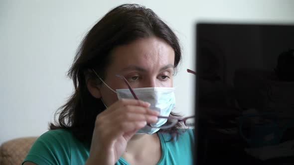 Stressful Woman Sitting in Mask Near Laptop and Reading New, Put of Glasses. Home Quarantine, Social