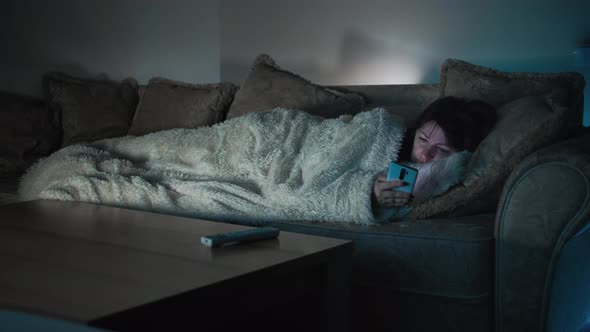 Sad Woman Lies on the Sofa in Front of Tv and Uses the Phone